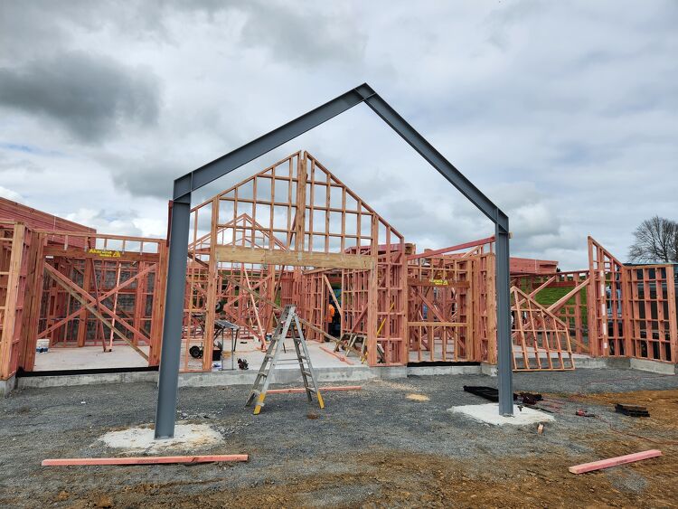 Timber house framing with exposed steel entrance frame under construction on a residential building site.