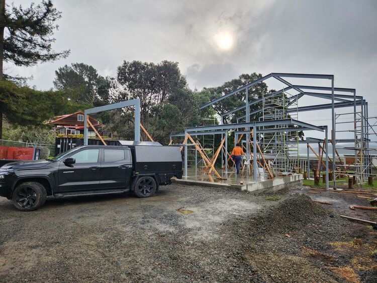 Steel frame structure under construction beside a utility vehicle with custom service body canopy.
