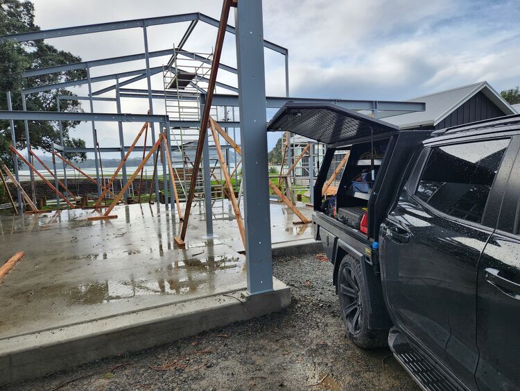 Structural steel framework being installed on a commercial building site with a utility service vehicle parked beside it.